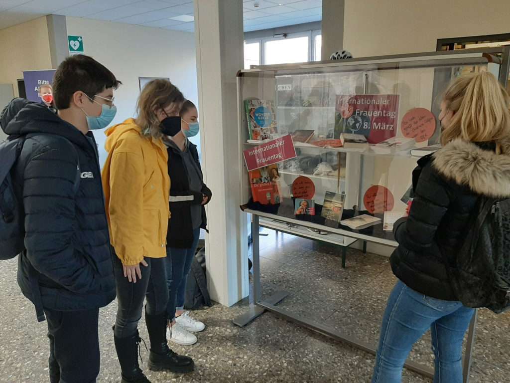 Schülerinnen und ein Schüler stehen vor dem Schaukasten der Schulbibliothek.