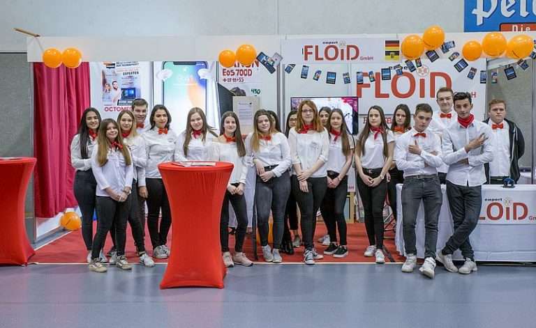Schülerinnen und Schüler stehen versammelt vor ihrem Messestand bei Übungsfirmenmesse RegioLahr.