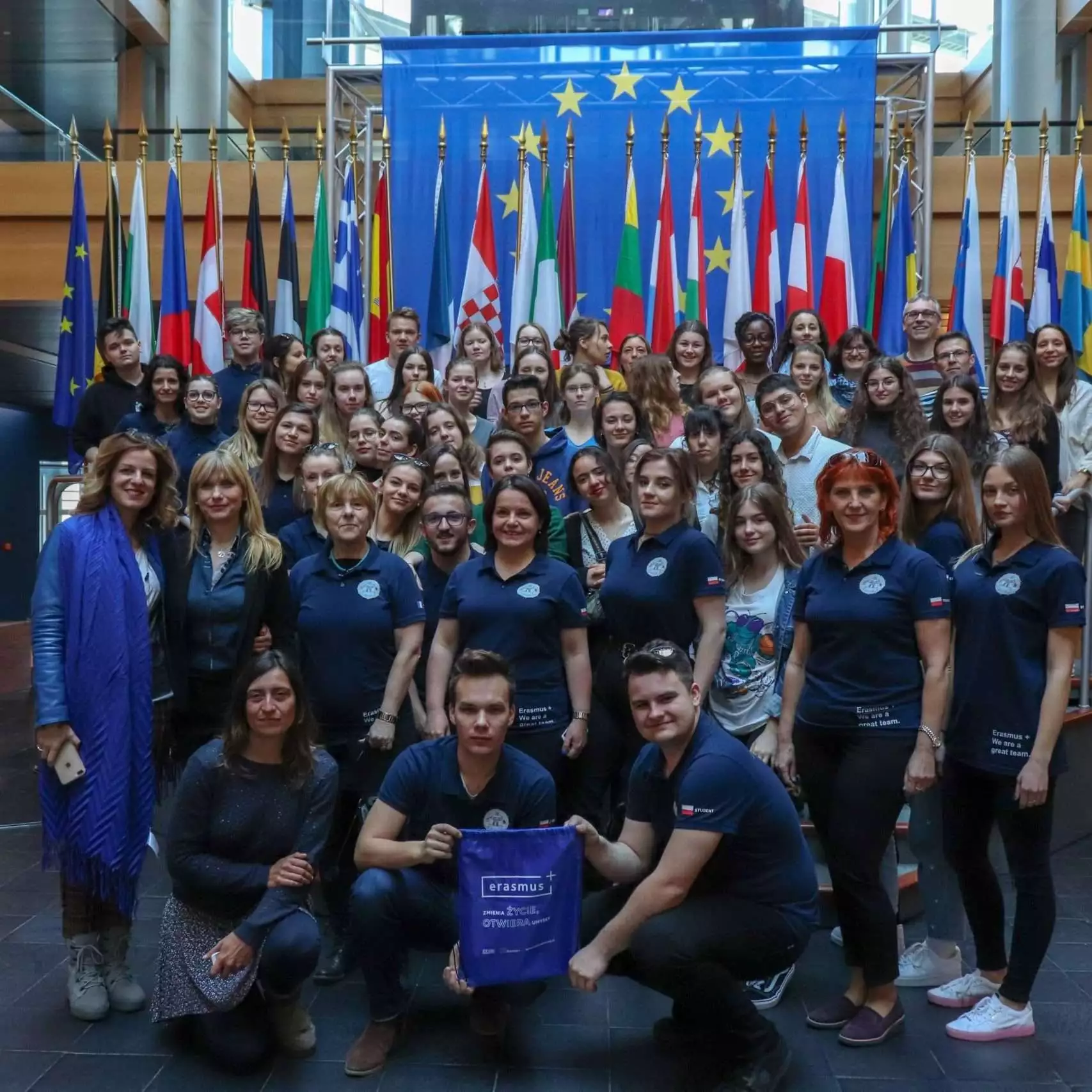 Lehrerinnen und Lehrer, Schülerinnen und Schüler stehen in einer großen Gruppe vor den europäischen Flaggen.